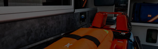 Fotografía de una camilla de rescate color naranja con una cinta color negro y franjas color amarillo y blanco.
