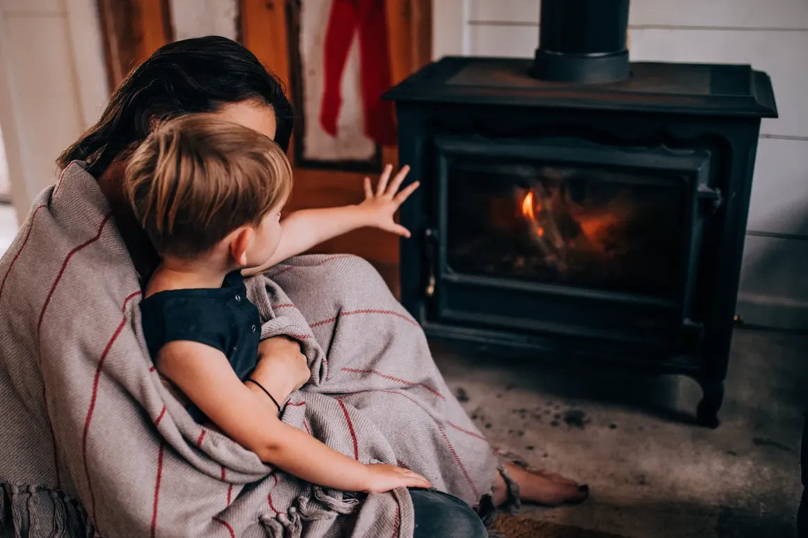 Cómo prevenir incendios en casa: Fotografía desde atrás de una mujer cargando a un niño frente a una chimenea.