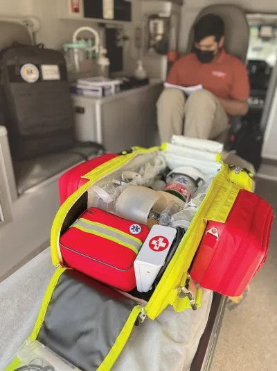 Fotografía desde arriba de una mochila color rojo con cierres y detalles amarillos abierta que contiene un kit de emergencia.