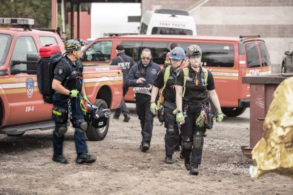 Fotografía de personas con equipos de protección y camisa negra en camino a brindar primeros auxilios básicos.