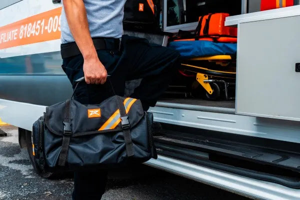 Equipo para paramédicos: fotografía de un hombre en la puerta de una ambulancia sosteniendo un maletín color negro.
