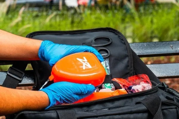 Fotografía de una persona utilizando guantes color azul mientras sostiene una mascarilla de RCP color naranja.