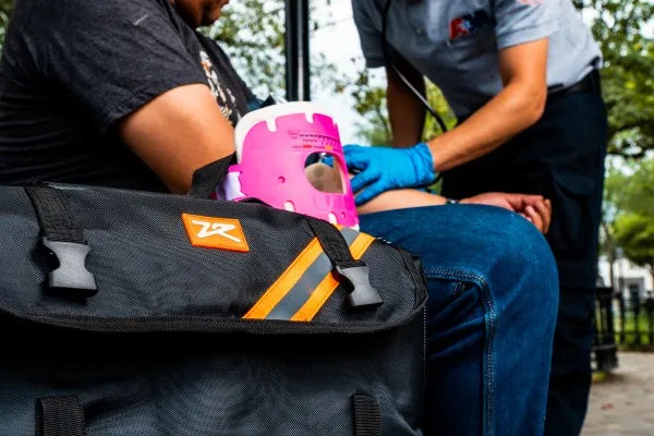 Fotografía de un paramédico brindando atención utilizando una mochila de trauma color negro con naranja.