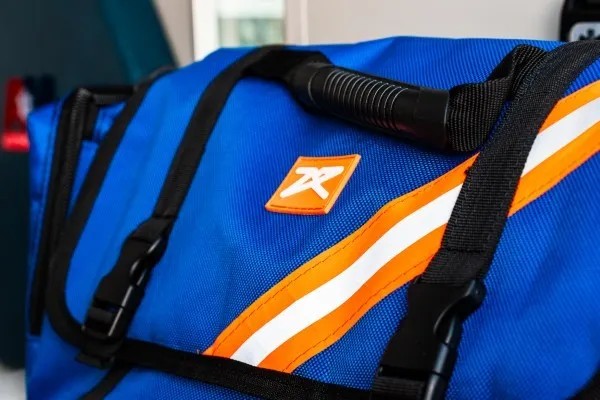 Fotografía de una mochila color azul con detalles en color negro, naranja y negro que contiene un kit de emergencia.