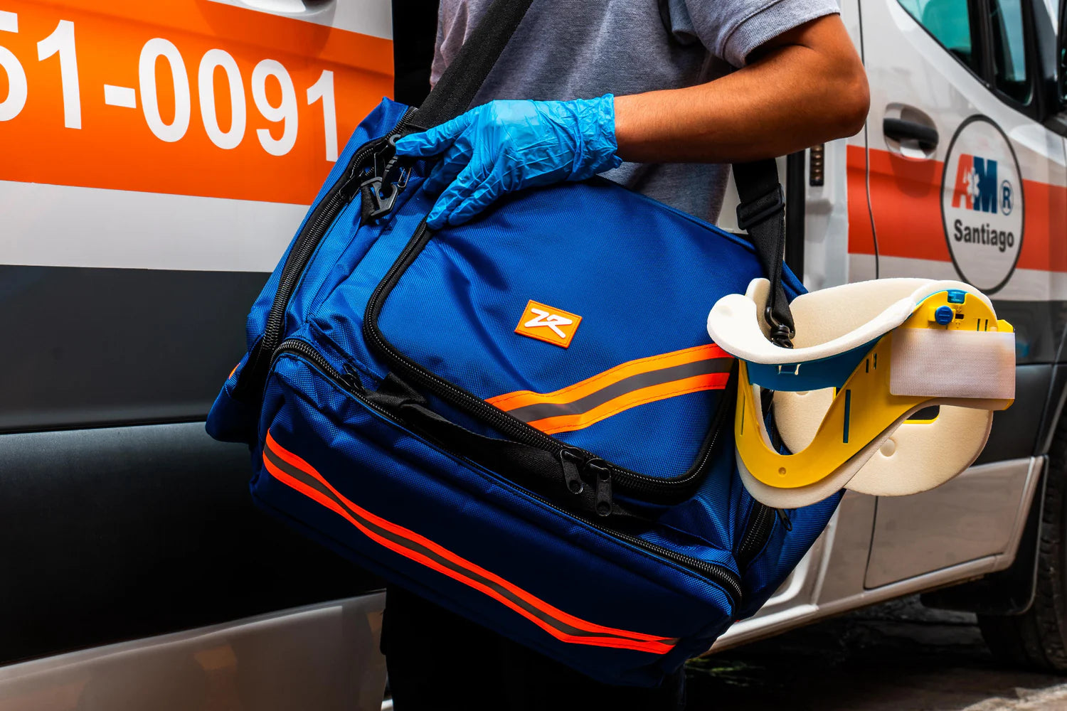 Hombre utilizando guantes y cargando una mochila color azul con detalles naranjas y negros que guarda equipos de emergencia.