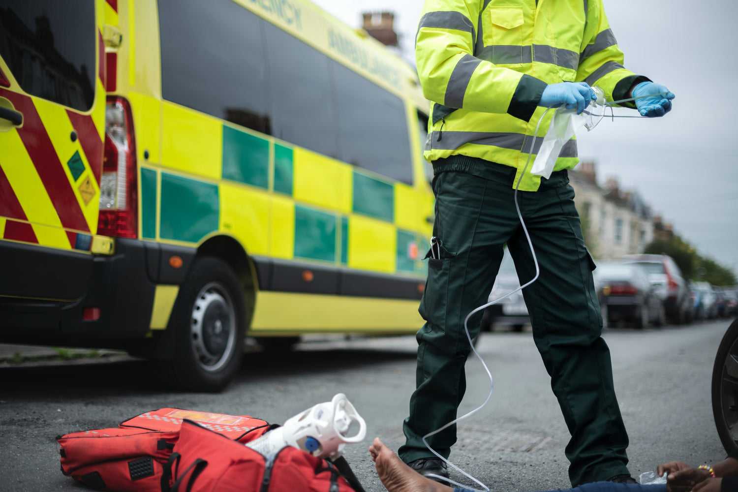Fotografía de un paramédico utilizando equipos de emergencia con uniforme color amarillo y una ambulancia atrás.