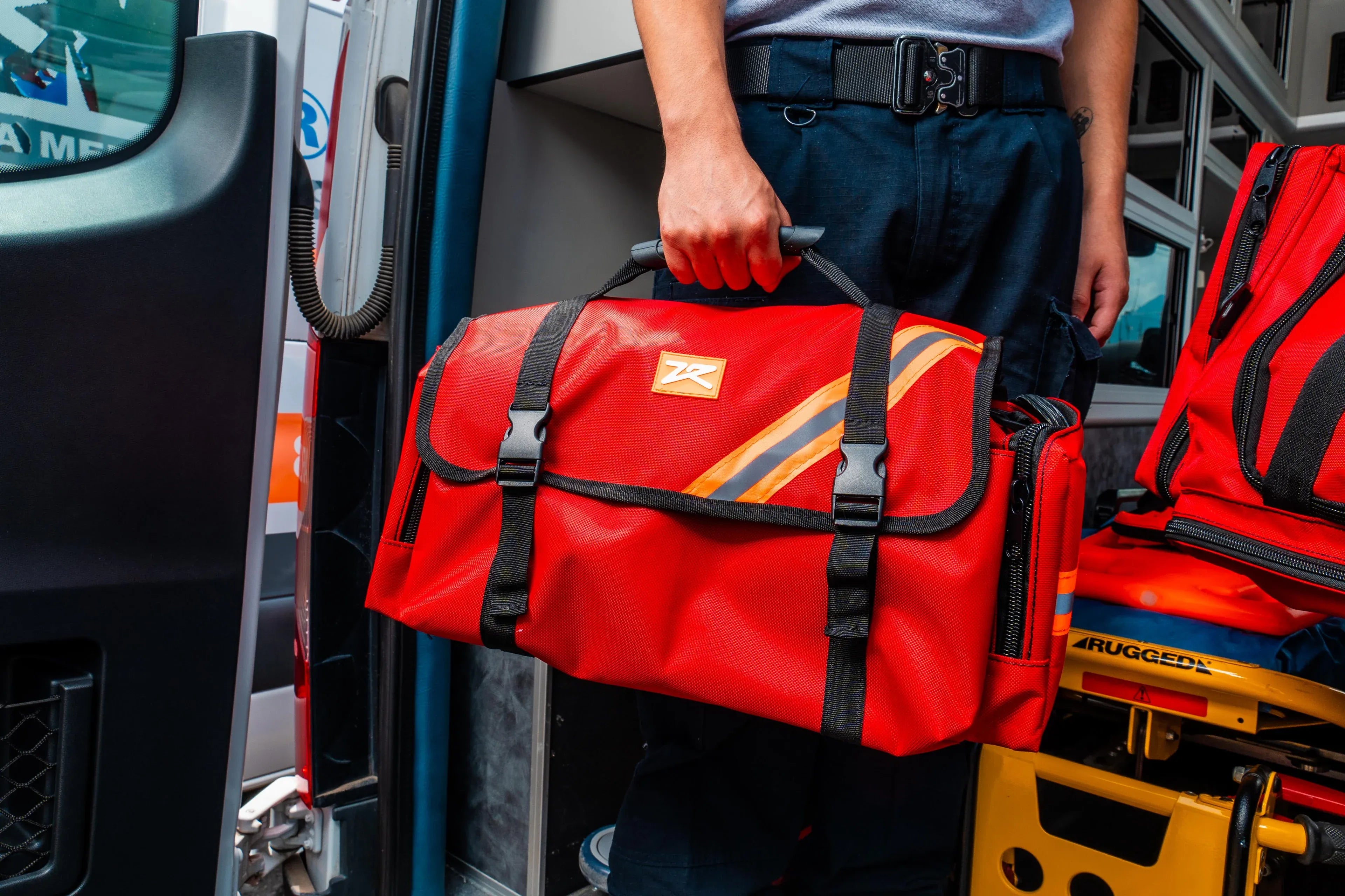 Fotografía de un hombre con uniforme sosteniendo un maletín rojo que contiene equipo médico de emergencia.