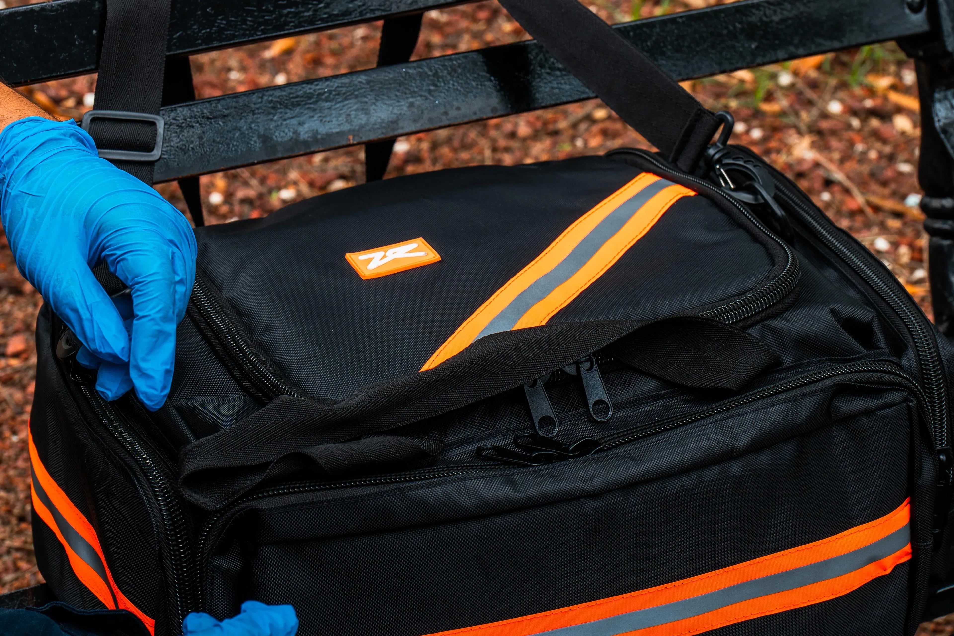Fotografía de una persona con guantes azules cerrando un maletón negro con naranja que guarda equipo médico de rescate.