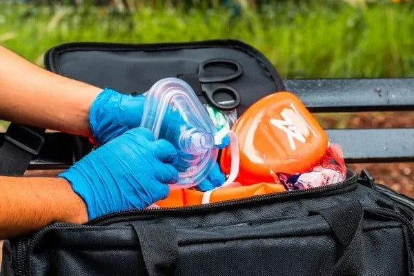 Fotografía de una persona usando guantes azules y sacando de un estuche color naranja una mascarilla de RCP transparente.