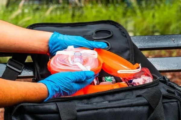 Fotografía de una persona sosteniendo un estuche color naranja que está abierto y contiene una mascarilla de RCP.