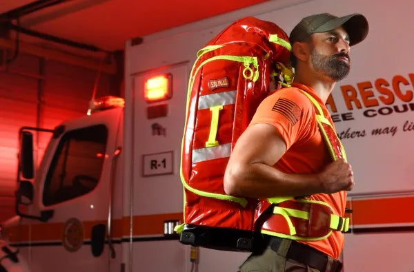 Equipo para paramédicos: fotografía de un hombre de camisa naranja y gorra portando una mochila color rojo.