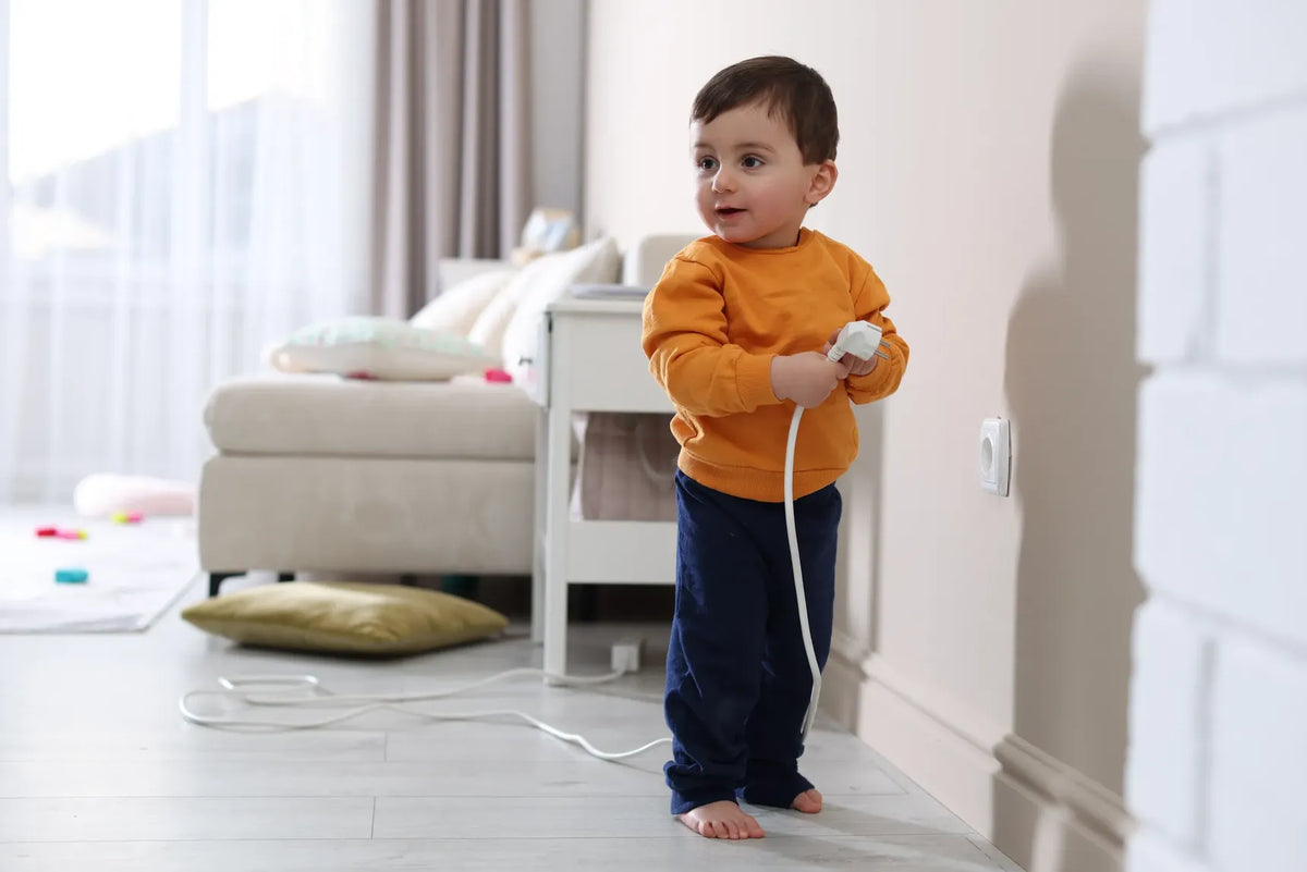 Seguridad para niños en casa: Fotografía de un niño con camisa color naranja sosteniendo un enchufe color blanco.