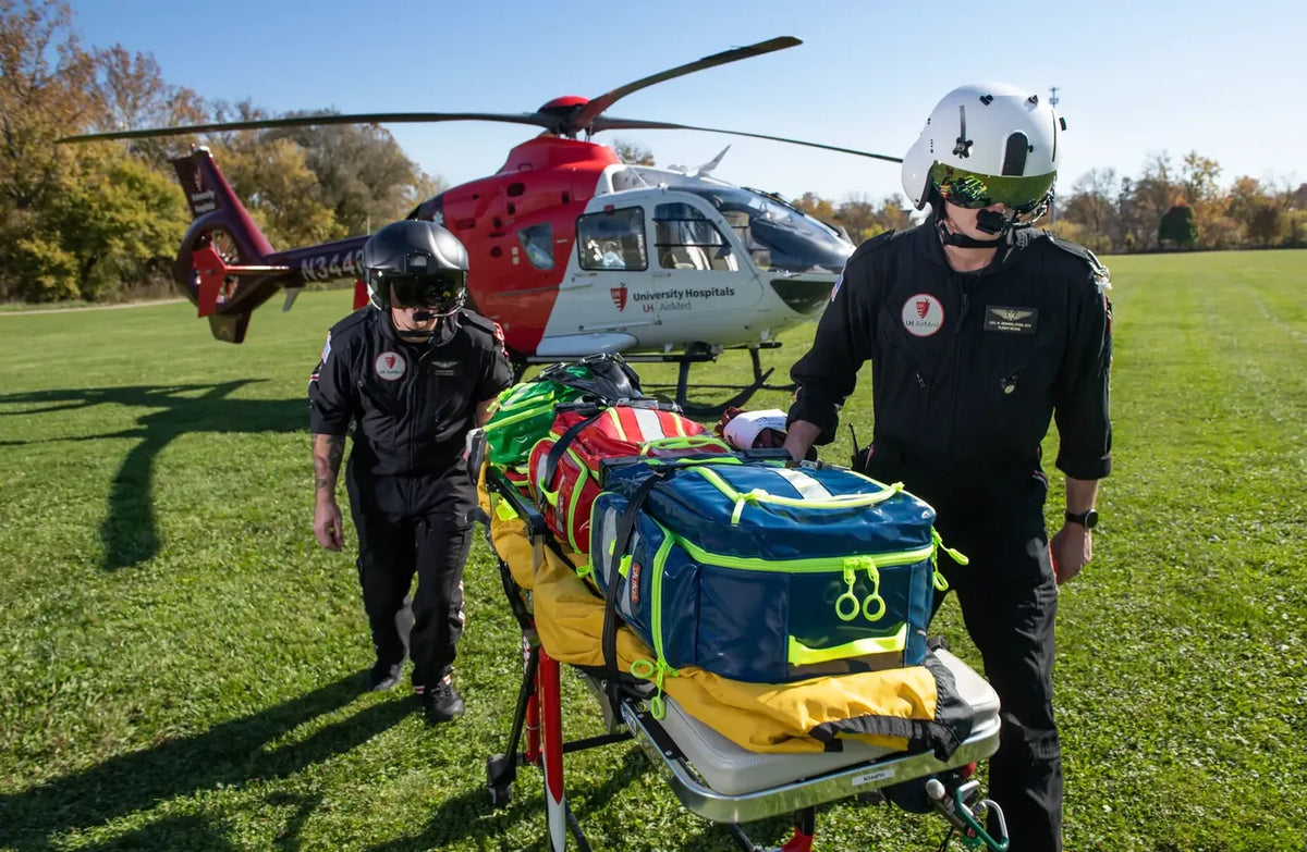 Triage qué es y para qué sirve: Fotografía de dos personas llevando una camilla con tres mochilas de primeros auxilios.