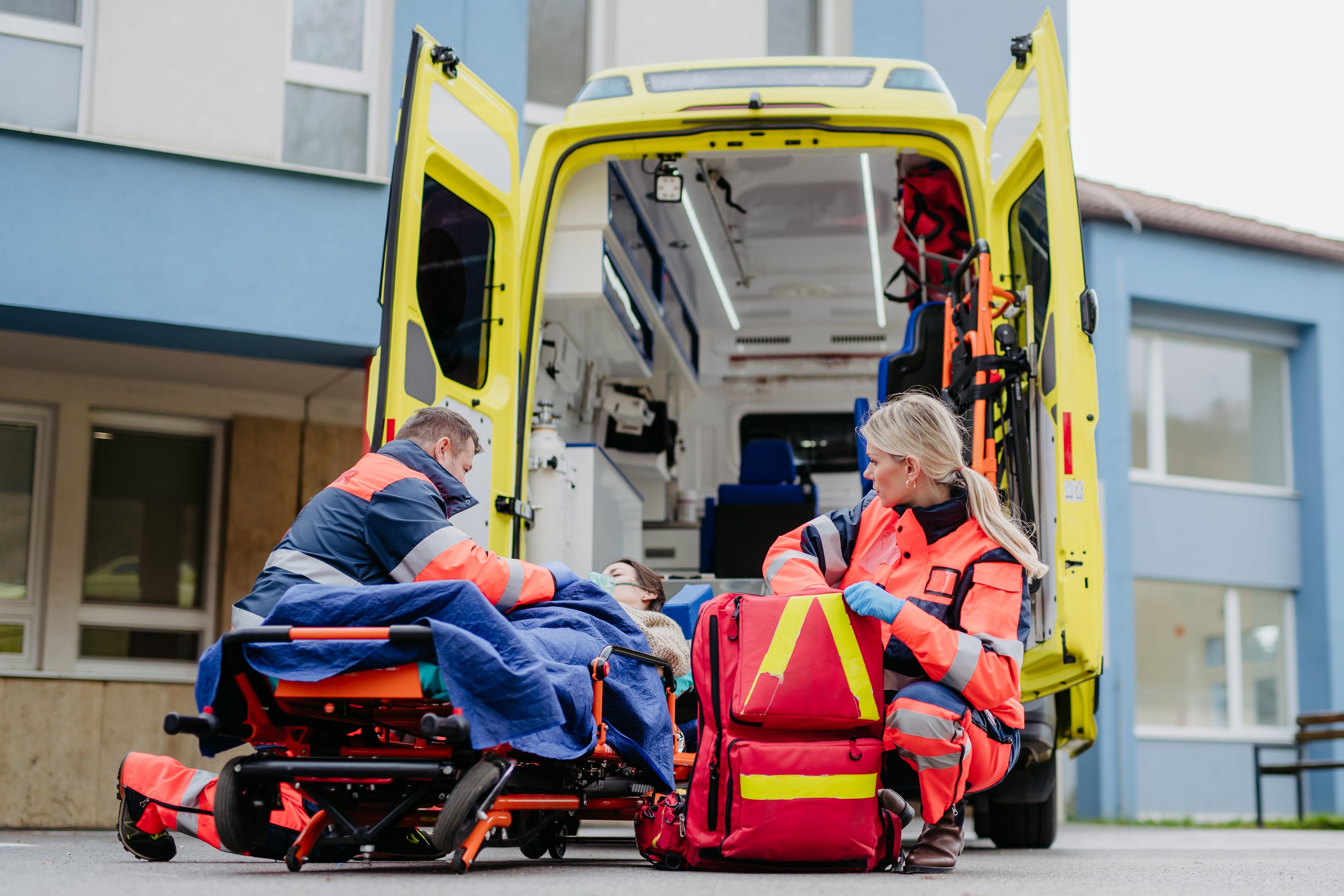 Fotografía de dos paramédicos afuera de una ambulancia atendiendo a un paciente usando kits de equipo de rescate.